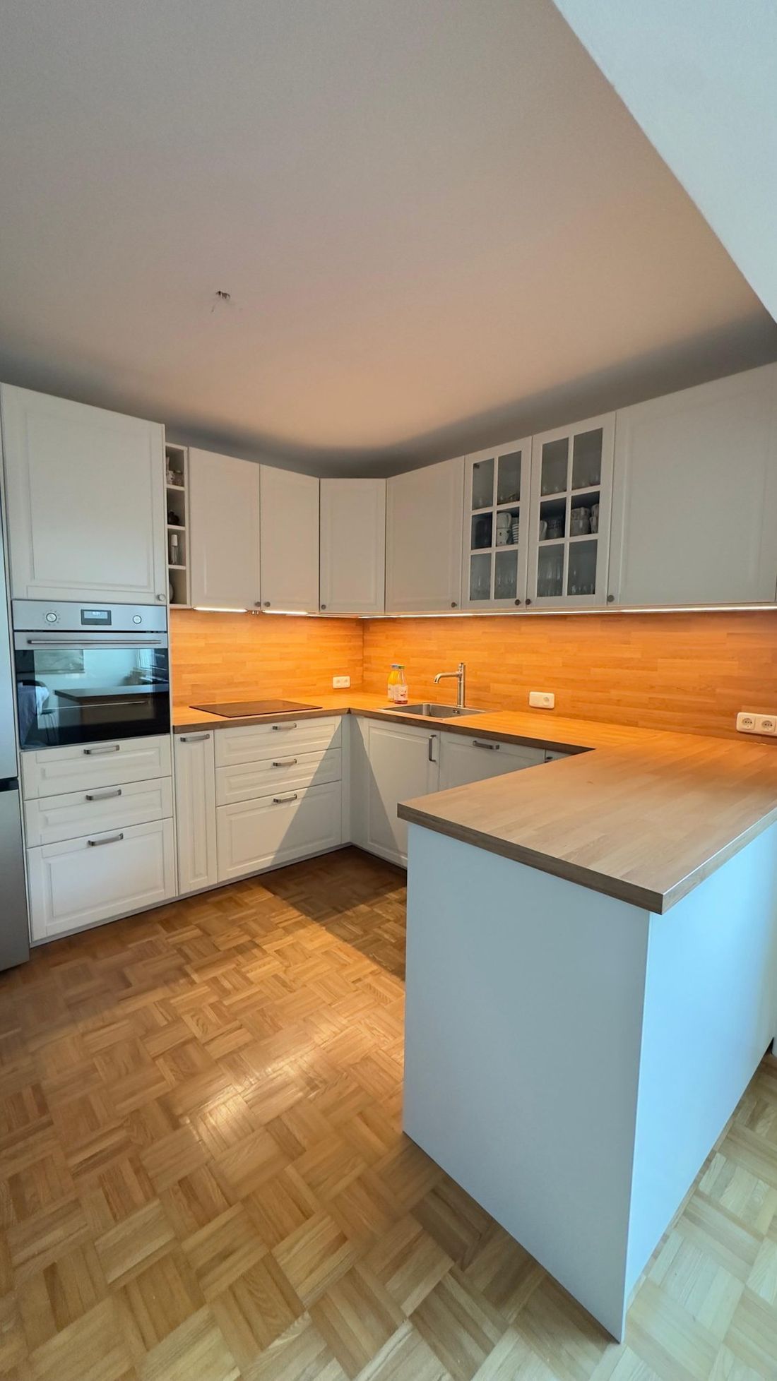 Weiße U-Küche mit Holzrückwand und Glasvitrinen